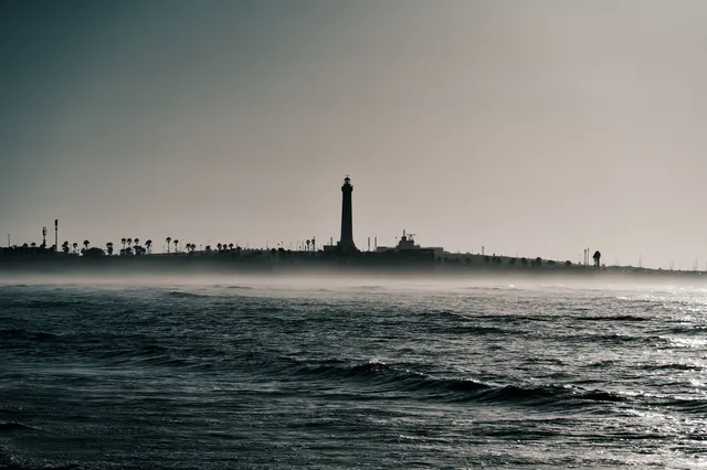 A lighthouse on the horizon behind sea mist and waves